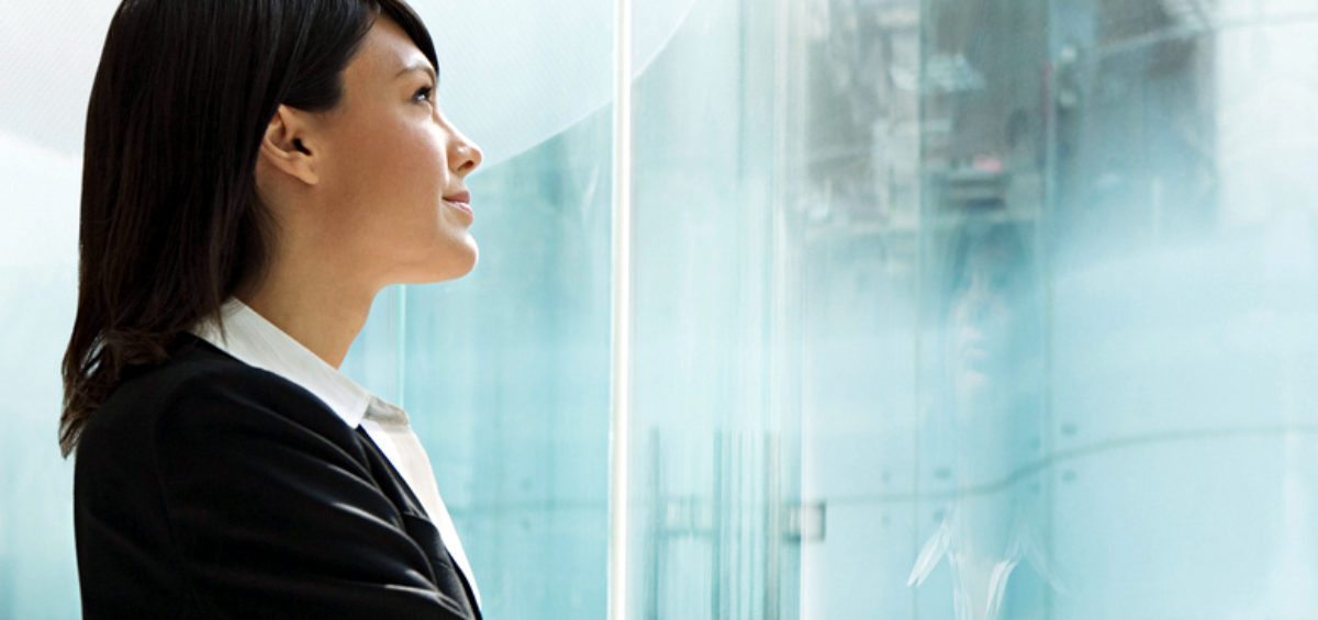 Corporate woman peering out full-length glass window, illustrating her successful personal brand